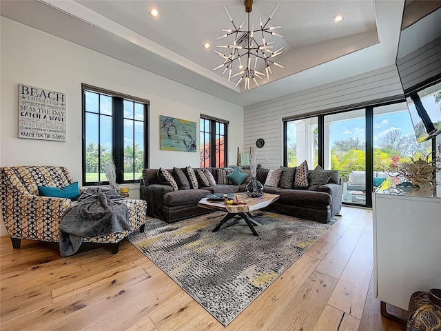 living room featuring a healthy amount of sunlight, an inviting chandelier, light hardwood / wood-style floors, and a tray ceiling