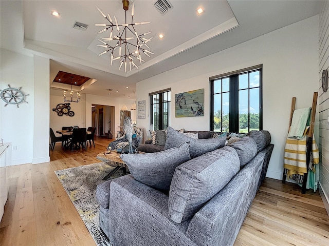 living room featuring light hardwood / wood-style flooring, french doors, a tray ceiling, and an inviting chandelier