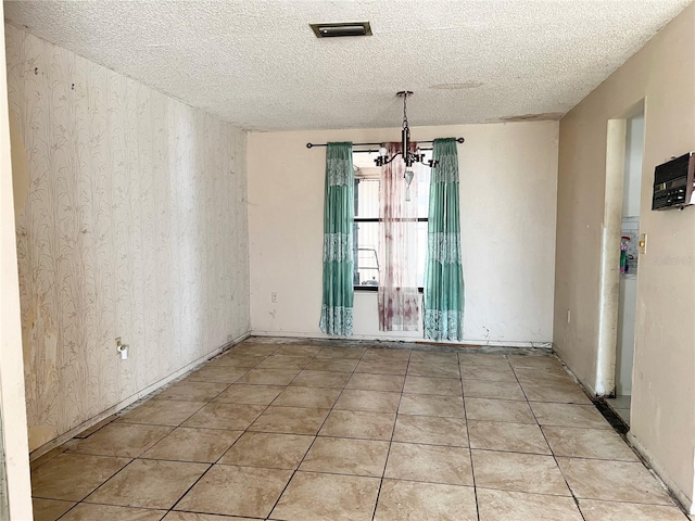 unfurnished room with an inviting chandelier, a textured ceiling, and light tile floors