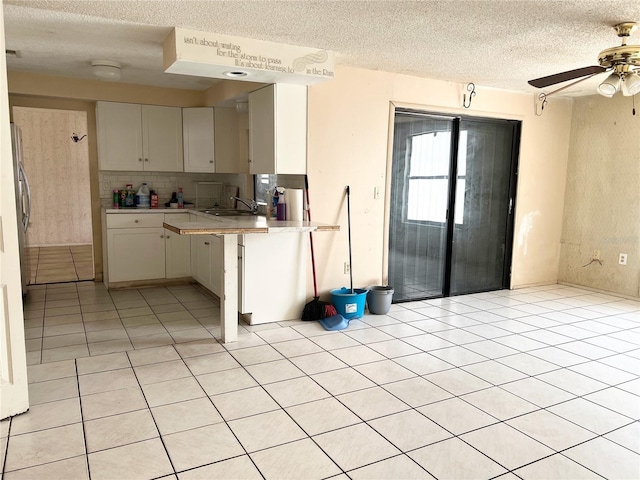 kitchen with ceiling fan, light tile floors, white cabinetry, sink, and a textured ceiling