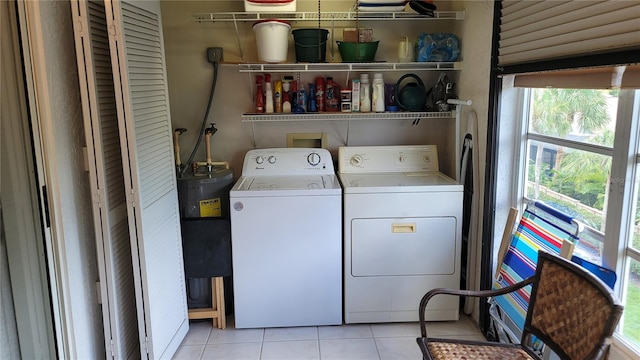 clothes washing area featuring light tile patterned floors, a wealth of natural light, washer and clothes dryer, and electric water heater