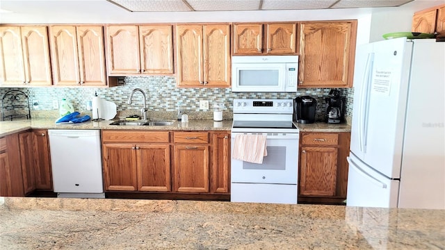 kitchen featuring backsplash, sink, light stone countertops, and white appliances