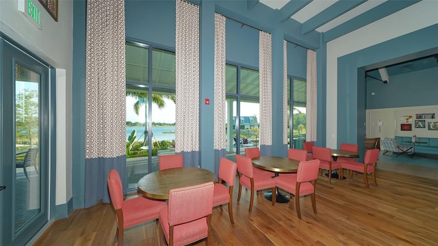 dining area with wood-type flooring, a water view, and a towering ceiling