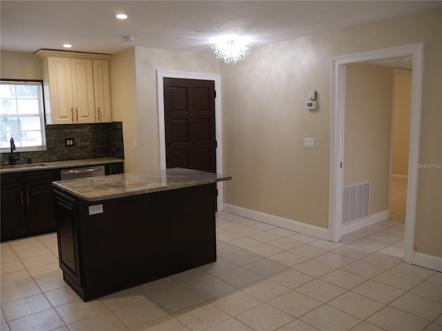 kitchen with light stone countertops, backsplash, sink, light tile patterned floors, and a center island