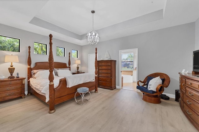 bedroom featuring light hardwood / wood-style flooring, a raised ceiling, connected bathroom, and a chandelier