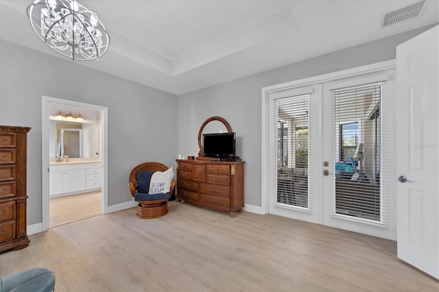 living area with a raised ceiling, light hardwood / wood-style floors, an inviting chandelier, and french doors