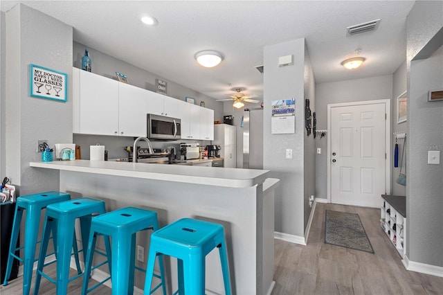 kitchen with a kitchen breakfast bar, light wood-type flooring, appliances with stainless steel finishes, kitchen peninsula, and ceiling fan