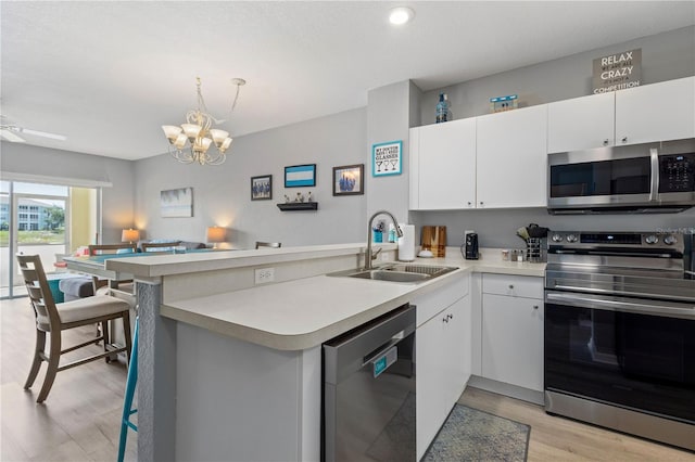 kitchen with ceiling fan with notable chandelier, stainless steel appliances, kitchen peninsula, light wood-type flooring, and sink