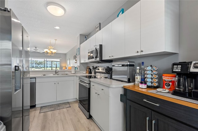 kitchen with hanging light fixtures, light hardwood / wood-style flooring, white cabinets, and appliances with stainless steel finishes