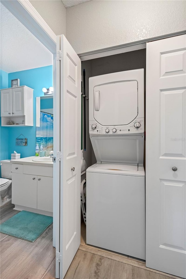 clothes washing area with stacked washer / dryer, light hardwood / wood-style floors, and sink