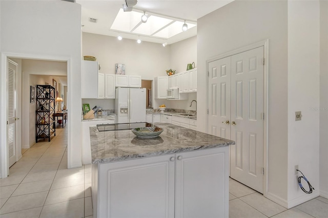 kitchen featuring a kitchen island, white fridge with ice dispenser, white cabinets, and light tile floors