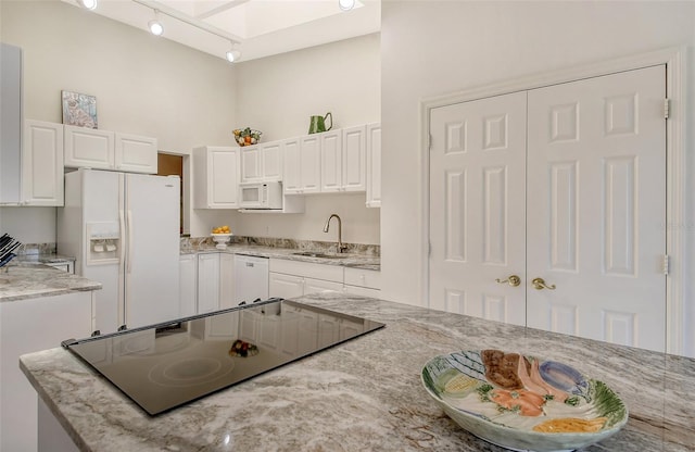 kitchen with light stone countertops, white appliances, white cabinetry, rail lighting, and sink