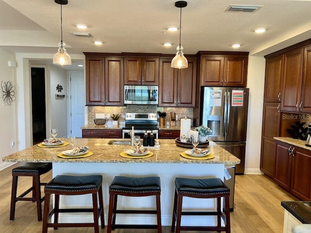 kitchen featuring a kitchen bar, appliances with stainless steel finishes, tasteful backsplash, light hardwood / wood-style floors, and an island with sink