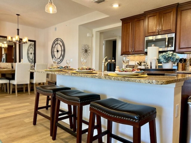 kitchen featuring an inviting chandelier, light hardwood / wood-style flooring, backsplash, pendant lighting, and a breakfast bar area