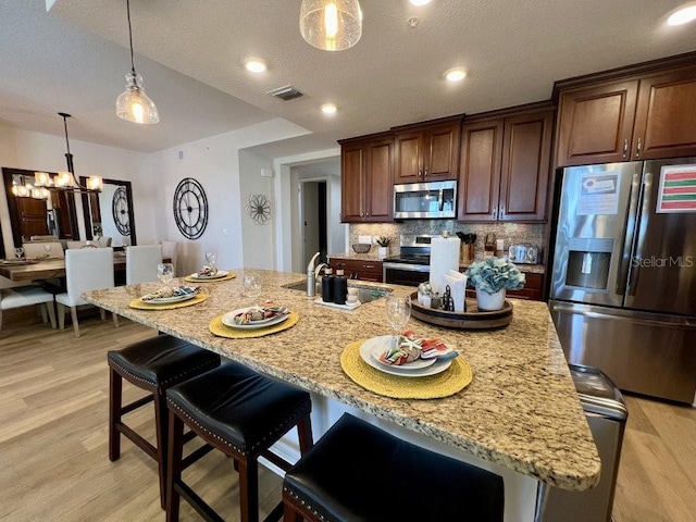 kitchen with a kitchen breakfast bar, sink, light wood-type flooring, an island with sink, and appliances with stainless steel finishes