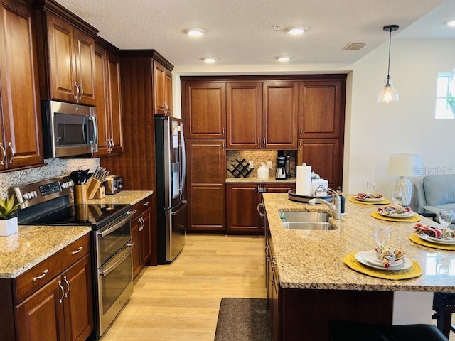 kitchen with backsplash, sink, hanging light fixtures, light wood-type flooring, and stainless steel appliances