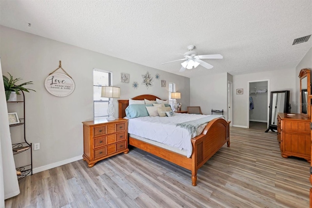 bedroom with ceiling fan, a spacious closet, a textured ceiling, light hardwood / wood-style floors, and a closet