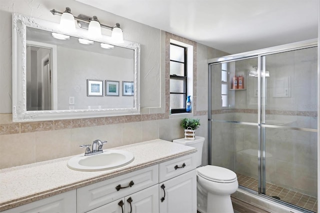 bathroom with vanity, toilet, tile walls, and a shower with shower door