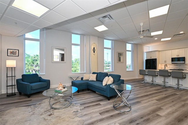 living room with ceiling fan, a drop ceiling, light hardwood / wood-style floors, and sink