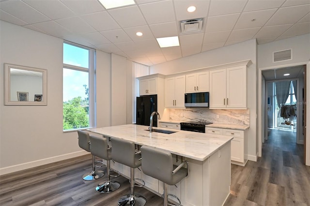 kitchen with light stone countertops, sink, black appliances, a center island with sink, and white cabinetry