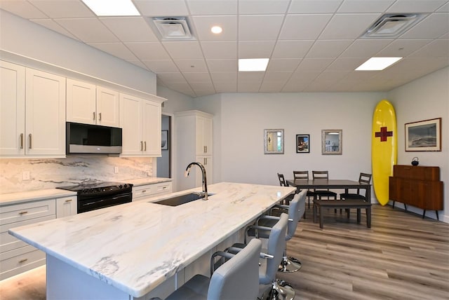 kitchen featuring a center island with sink, white cabinetry, sink, and black electric range