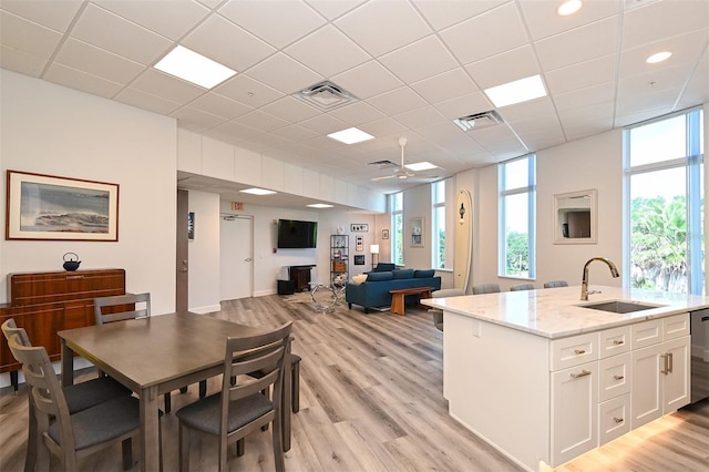 interior space with sink, light stone counters, light hardwood / wood-style flooring, a kitchen island with sink, and white cabinets