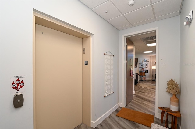 hallway featuring a paneled ceiling, light hardwood / wood-style floors, and elevator