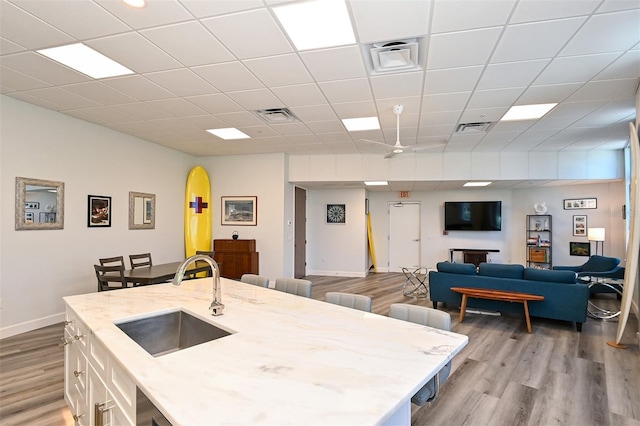 kitchen featuring light wood-type flooring, light stone counters, a breakfast bar area, and sink