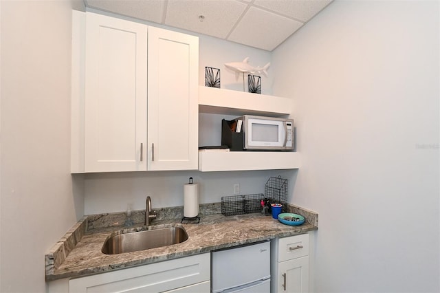 kitchen featuring white cabinets, a drop ceiling, dark stone countertops, and sink