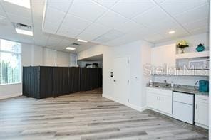 bar featuring a paneled ceiling, white cabinetry, sink, and light hardwood / wood-style flooring