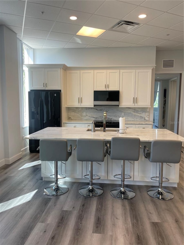 kitchen with a kitchen bar, white cabinetry, and black refrigerator with ice dispenser