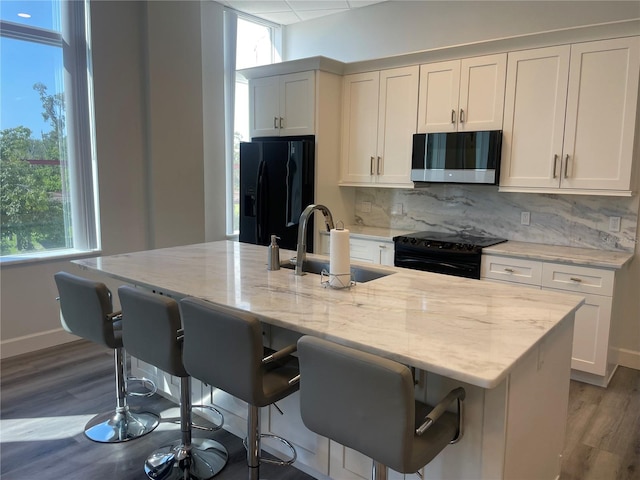 kitchen with black appliances, a kitchen breakfast bar, sink, an island with sink, and light stone counters