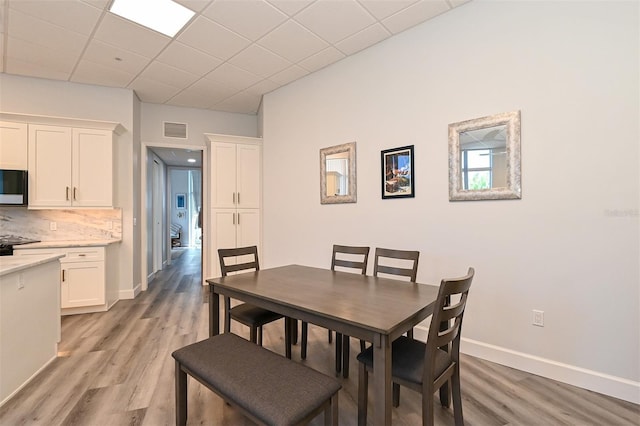 dining area with a drop ceiling and light wood-type flooring