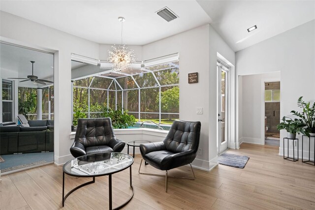 sitting room featuring light wood-type flooring, vaulted ceiling, and ceiling fan with notable chandelier