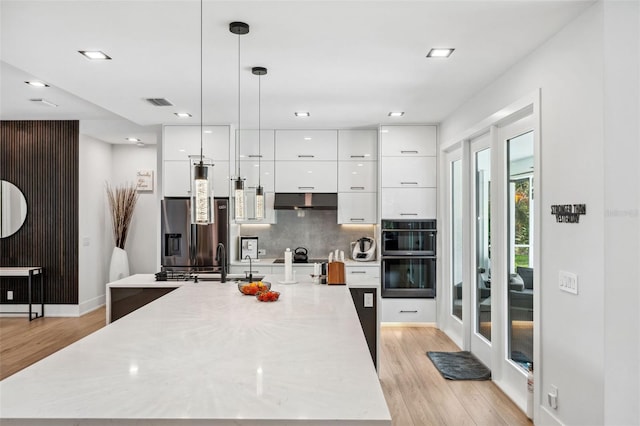 kitchen with white cabinets, light wood-type flooring, sink, stainless steel refrigerator with ice dispenser, and a center island with sink