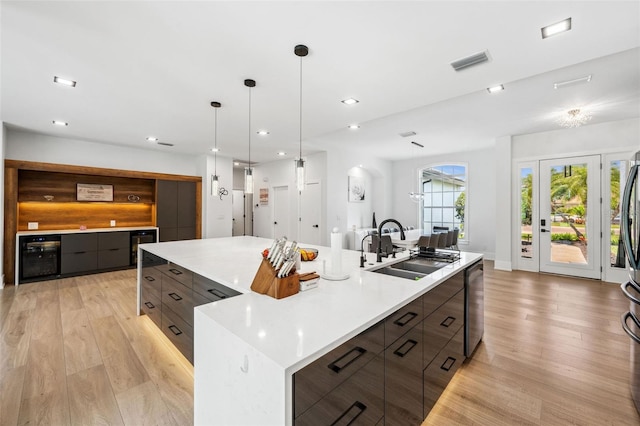 kitchen featuring a large island with sink, light hardwood / wood-style flooring, dishwasher, beverage cooler, and sink