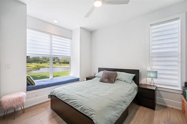 bedroom featuring light hardwood / wood-style flooring, ceiling fan, and a water view