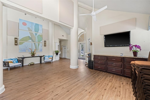 living room with high vaulted ceiling, ornate columns, ceiling fan, and light hardwood / wood-style flooring