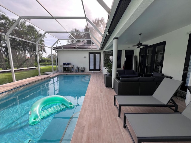 view of pool with glass enclosure, area for grilling, outdoor lounge area, and ceiling fan