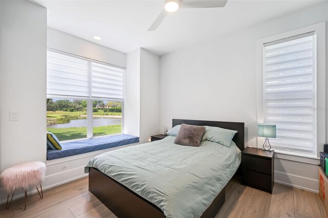 bedroom featuring baseboards, a ceiling fan, wood finished floors, and a water view