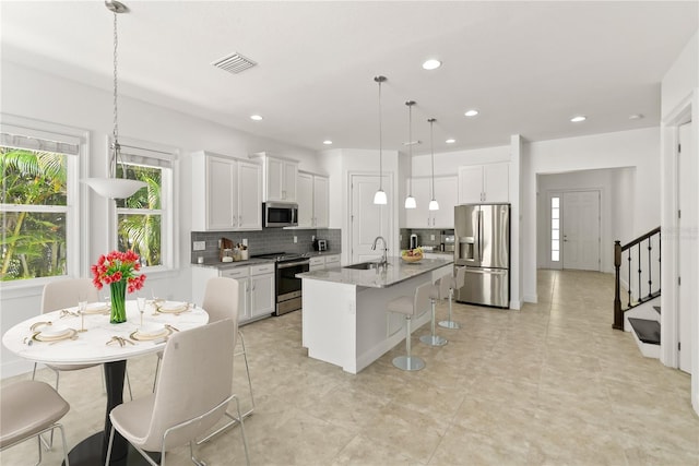 kitchen featuring white cabinetry, stainless steel appliances, a kitchen island with sink, hanging light fixtures, and sink