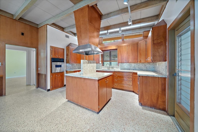 kitchen featuring a center island, beam ceiling, stainless steel oven, sink, and tasteful backsplash