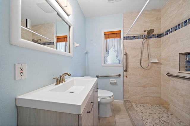 bathroom with toilet, tile flooring, vanity, and a tile shower