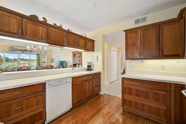 kitchen with light wood-type flooring, sink, a textured ceiling, and white dishwasher