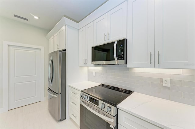 kitchen featuring appliances with stainless steel finishes, light tile flooring, backsplash, white cabinetry, and light stone countertops