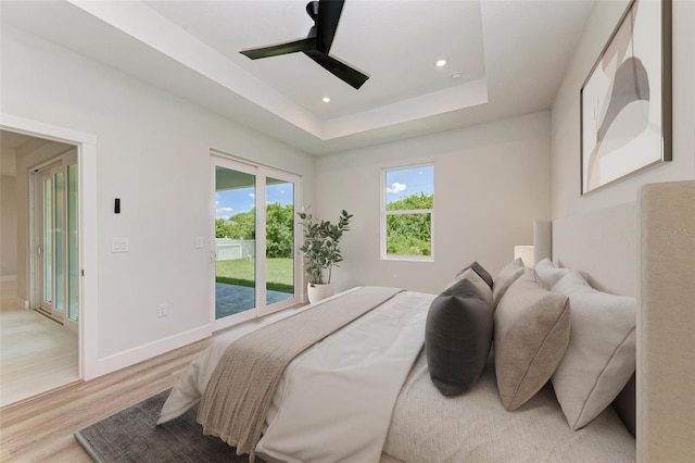 bedroom with hardwood / wood-style floors, ceiling fan, a tray ceiling, and access to exterior