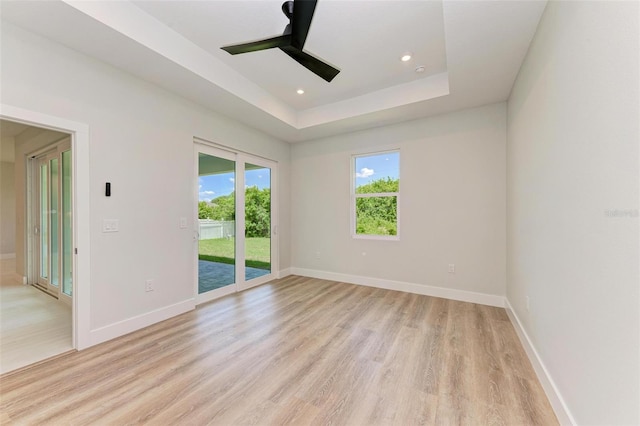 empty room with a raised ceiling, ceiling fan, and light wood-type flooring