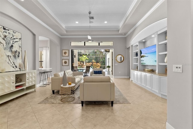 tiled living room with a tray ceiling, built in features, ceiling fan, and ornamental molding