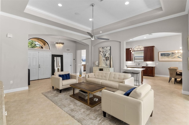 tiled living room featuring ceiling fan with notable chandelier, crown molding, and a tray ceiling