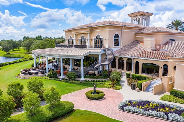 back of property with a lawn, a balcony, and a water view